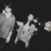 The monochrome photo of the three men of Dhidalah seems to be taken outside during nighttime. The photo has some blurring effect as if the musicians have moved a bit while the photo was taken or this is a combination of two photos. Photography by Kentaro Takahashi