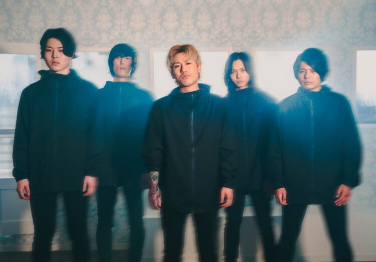 The photo depicts members of the band Sailing Before The Wind standing in a line in a room, behind them there are windows. All are dressed in the same black attire, wearing black pants and jackets.