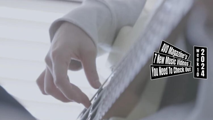 Still from the music video "おかえり (Okaeri)" by ベンチウォーマーズ (Bench Warmers). One of the band members is playing her bass guitar in the corner of a very light and white room. The still is zoomed in on the right hand of the musician.