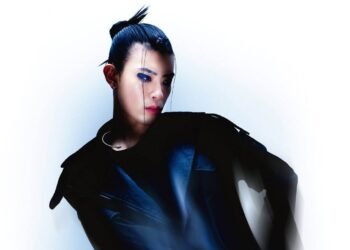 Tohji stands against a white background while wearing black-coloured clothing and his hair in a knot. Photo by Nikita Ono and styling by Luca Wowczyna