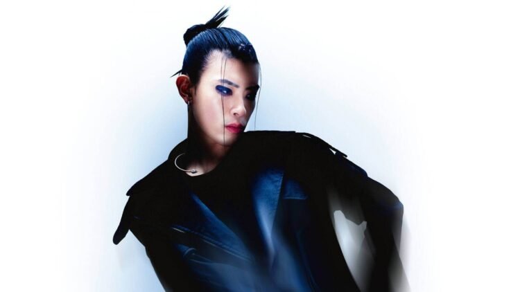 Tohji stands against a white background while wearing black-coloured clothing and his hair in a knot. Photo by Nikita Ono and styling by Luca Wowczyna