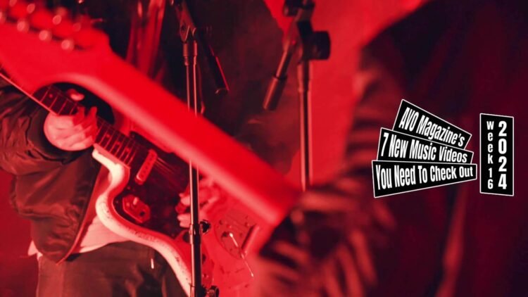 Still from ĀTMAN's music video for "反撃 (Counterattack)". The vocalist and guitarist of ĀTMAN is in the still, although the focus lies onto his electric guitar and the mirror image of it. The still also shows a bit of the microphone stand and the back of the musician. The lighting that they have used for this part of the still is red of colour. The video is directed by Akari Kinjo, camera work and lighting is done by Mayu Uchida, assisted by Mahiro Fukano and Nanai Saito.