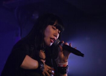 The photo depicts the solo idol Himari Tsukishiro performing a live show on the stage of Tin Arts, she is dressed in black attire and has long black hair.