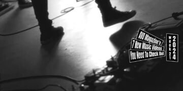 Still from DRAW INTO DISORDER's music video for the song "Dying country". The still is a black and white image of several people standing on a floor, but the still focuses primarily on the legs of the musicians that are in the middle of a performance and a guitar pedal board.