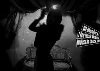 Still from Remnant's music video for the song "Re:Incarnation". The still features silhouettes of Remnant's three band members, they are standing in a dimly lit room with a sofa against the wall. The still is a bit blurry as they are moving in the still which adds a spooky element.