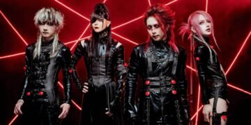 The photo depicts the four band members of JILUKA standing in a row surrounded by red lights shining from different angles, creating a mysterious and lively atmosphere. The lighting in the picture is also often used at concerts or dance parties. All band members are dressed in black clothing that seems to be leather or leather-like.