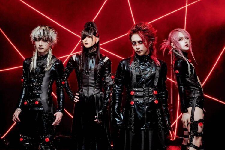 The photo depicts the four band members of JILUKA standing in a row surrounded by red lights shining from different angles, creating a mysterious and lively atmosphere. The lighting in the picture is also often used at concerts or dance parties. All band members are dressed in black clothing that seems to be leather or leather-like.