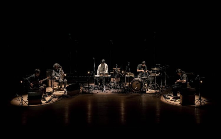 goat on stage in 2023. It features the five members of goat engaging in a performance while sitting in a semicircle setting. Photo: Yoshikazu Inoue