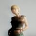 The photo features Nao Yoshioka with blonde hair posing in a studio setting. She is wearing a black crop tank top and green trousers. There is an effect added to the photo giving an idea of movement and blurriness.