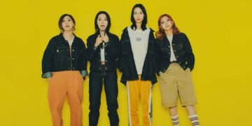 The photo features four members of Bray me standing in front of a yellow background. Each member has a distinct fashion style and is striking a different pose.