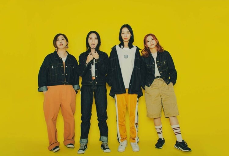 The photo features four members of Bray me standing in front of a yellow background. Each member has a distinct fashion style and is striking a different pose.