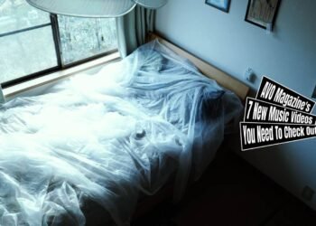 Still of the music video "eureka" by the band bakeru.., directed by Mei Kawaguchi. The still depicts a bedroom featuring a bed decorated with sheer sheets/curtains. To the right is a wall with photo frames and paper memorandums and on the left is a window with a view to a garden.