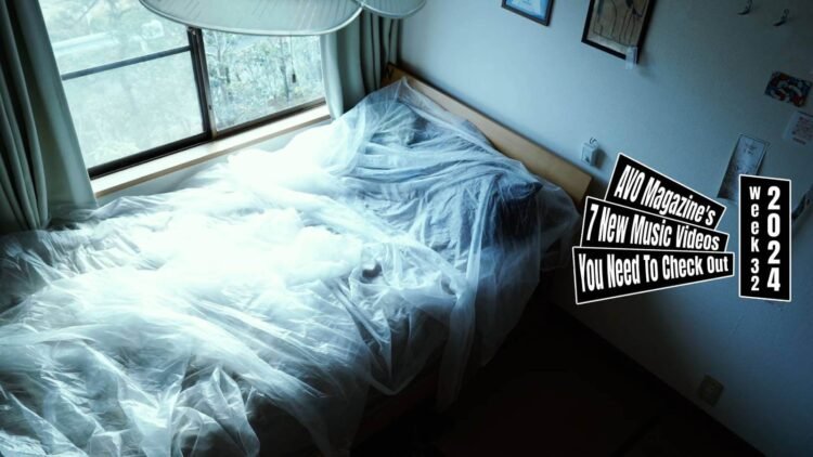Still of the music video "eureka" by the band bakeru.., directed by Mei Kawaguchi. The still depicts a bedroom featuring a bed decorated with sheer sheets/curtains. To the right is a wall with photo frames and paper memorandums and on the left is a window with a view to a garden.