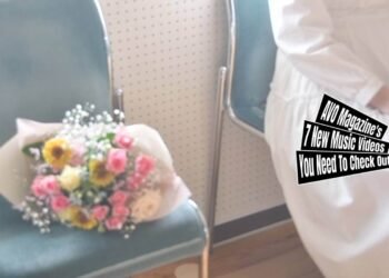Still from April After All's music video for the song "march". A lady dressed in a white dress is sitting on a green chair and next to her is a bouquet of colourful flowers. They are sitting next to a window that gives a lot of light and creates a hazy atmosphere as it the camera is overexposed. The filming and editing is done by one of the members of the band, Muneda.