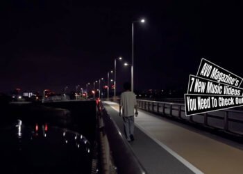 Still from the music video "戦争 (Fight)" by バカ力 (Bakadikara), directed by Hiroki Kurihara. A person is seen walking away from the camera on a road next to a body of water at night, evoking a sense of solitude.