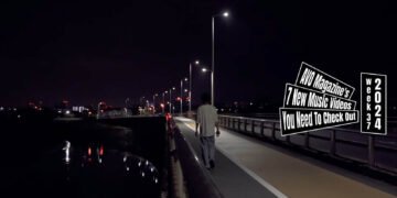 Still from the music video "戦争 (Fight)" by バカ力 (Bakadikara), directed by Hiroki Kurihara. A person is seen walking away from the camera on a road next to a body of water at night, evoking a sense of solitude.