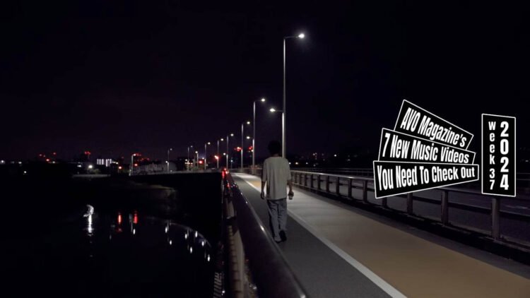 Still from the music video "戦争 (Fight)" by バカ力 (Bakadikara), directed by Hiroki Kurihara. A person is seen walking away from the camera on a road next to a body of water at night, evoking a sense of solitude.