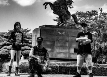 Black and white photo of the three-piece Kruelty standing in front a statue of a samurai on a rearing horse. Photography by Seijiro Nishimi (@/seijiro243)