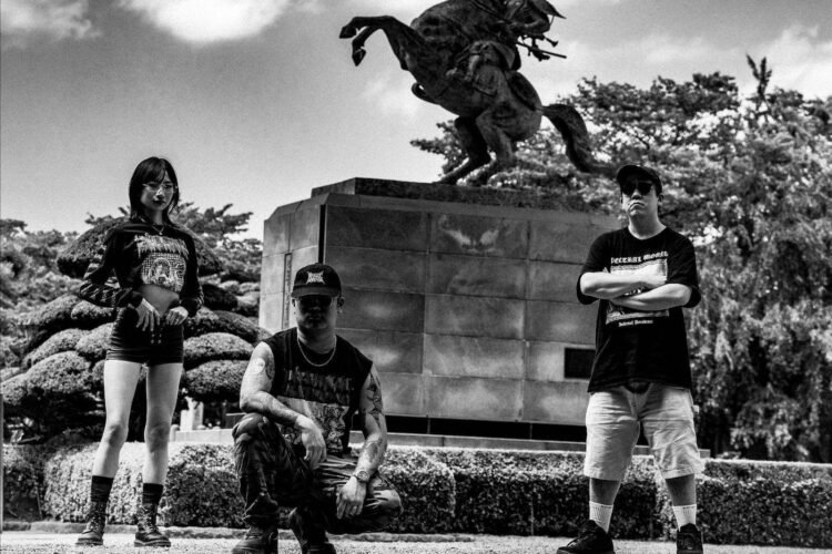 Black and white photo of the three-piece Kruelty standing in front a statue of a samurai on a rearing horse. Photography by Seijiro Nishimi (@/seijiro243)