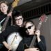The photo features a group photo of three women of the garage rock band The 5.6.7.8’s, each holding a different musical instrument and wearing the same sparkly black outfits. © The 5.6.7.8's