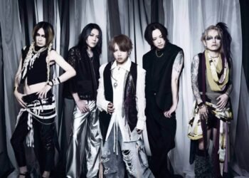 Band photo of Nightmare where the five members are each exhibiting distinct fashion styles and personalities. They are standing side by side in front of a background with alternating white, grey and black curtains.