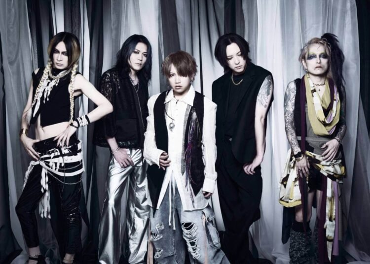 Band photo of Nightmare where the five members are each exhibiting distinct fashion styles and personalities. They are standing side by side in front of a background with alternating white, grey and black curtains.