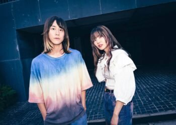 Band photo of SpecialThanks with Takaaki Yoshida and Misaki Anita standing on a place with stone tiles. Takaaki is wearing a tie-dye shirt and Misaki is wearing a white blouse and jeans.