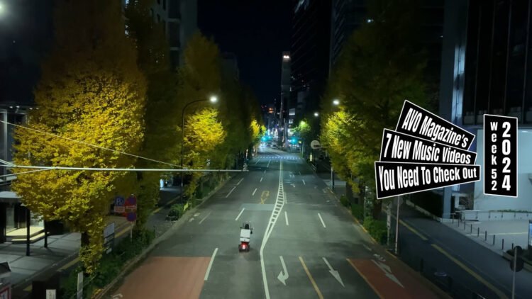 Still from Giraffe John's video for the song "Song to live". The still shows the last scene of the lyric video, a street during night time. A scooter rider just drives by while you can see the yellowed leaves of the trees lighten up by street lights.