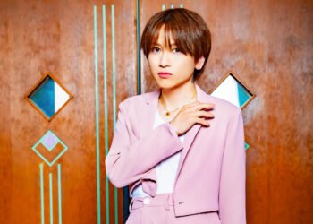 An Cafe's Miku posing in a light/old pink suit against a wooden wall.