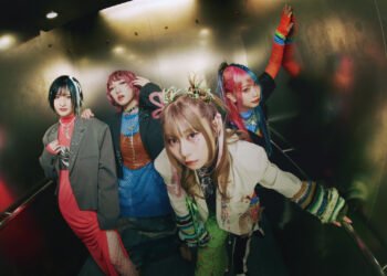 The photo shows the four members of HANABIE. posing together in an elevator. Each band member is distinctly dressed in colourful and unique outfits. From left to right: drummer Chika, guitarist/vocalist Matsuri, vocalist Yukina, and bassist Hettsu.