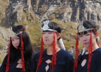 Photo of the tree ladies of KUUNATIC standing side by side wearing black dressed and silver headpieces and red cords that seem to be an artistic and symbolic interpretation, maybe inspired by sjamanistic or tribal styles. Photography by Celine Fougerouse