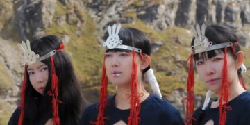 Photo of the tree ladies of KUUNATIC standing side by side wearing black dressed and silver headpieces and red cords that seem to be an artistic and symbolic interpretation, maybe inspired by sjamanistic or tribal styles. Photography by Celine Fougerouse