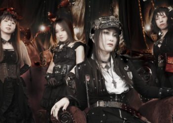 The photo shows the steampunk metal band FATE GEAR, dressed in dark gothic and steampunk inspired fashion. The bandleader, 'Captain' Mina, sits in front of the other three standing members.