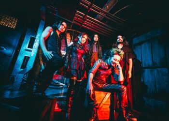 The photo depicts the members of FATHOMLESS SKYWALKER dressed in a gothic-inspired metal style in a dark lit room, probably located in an (old) factory with red lighting to amplify the atmosphere.