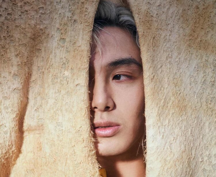 On the photo features the singer-songwriter and pianist Fujii Kaze peeking through yellow or gold-coloured textile cloth. Part of his face is visible, including his left eye looking away from the camera. This photo was used in the announcement for the European Tour 2025 of Fujii Kaze.