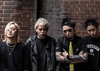 The photo features the four members of the Japanese band SiM (Silence iz Mine), all dressed in black attire and posing in front of a red brick wall.