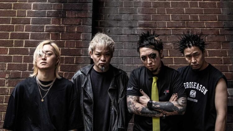The photo features the four members of the Japanese band SiM (Silence iz Mine), all dressed in black attire and posing in front of a red brick wall.