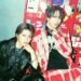 This photo features two musicians, Shou (Verde/, Alice Nine) wearing a black leather jacket and Takeru (ex-SUG) dreassed in an outfit with red and white stripes and a black shirt. They are sitting in front of red lockers that are covered with various stickers. © Takuma Hongo/Ryota Nakano