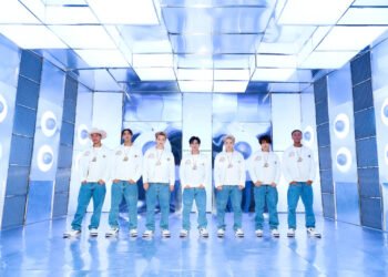 Group photo of PSYCHIC FEVER from EXILE TRIBE with the seven members of the group standing next to eachother, dressed uniformly in white sweatshirts and blue jeans. They are standing in a futuristic-looking room where the colour blue is predominantly present.