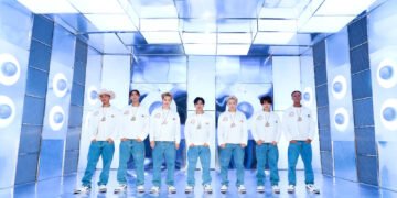 Group photo of PSYCHIC FEVER from EXILE TRIBE with the seven members of the group standing next to eachother, dressed uniformly in white sweatshirts and blue jeans. They are standing in a futuristic-looking room where the colour blue is predominantly present.