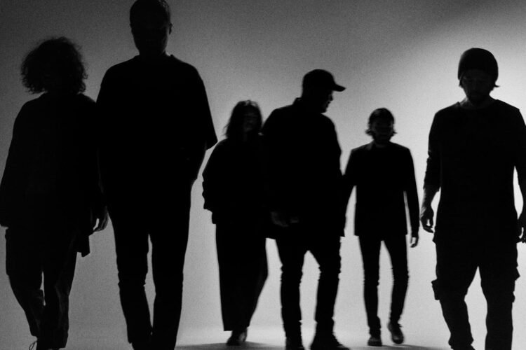 The (monochrome) photo shows the silhouettes of the six band members of envy standing in a row, walking forward.