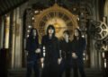 Photo of the four-piece alternative metal band Esprit D'Air standing side by side against a background featuring a large clockwork mechanism with gears, cogs, and springs, in golden/metallic tones. All members are dressed in dark clothing and standing in what seems to be an old clock tower. The same location and imagery can be seen in the music video for "Shadow of Time", which is produced by Mind Art Visual.