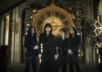 Photo of the four-piece alternative metal band Esprit D'Air standing side by side against a background featuring a large clockwork mechanism with gears, cogs, and springs, in golden/metallic tones. All members are dressed in dark clothing and standing in what seems to be an old clock tower. The same location and imagery can be seen in the music video for "Shadow of Time", which is produced by Mind Art Visual.