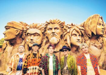 Pictured are the five members of FLOW in colourful clothing in front of the giant Hogake Rock at the Nijigen no Mori theme park. © AMUSE INC. (Naruto franchise ©2002 MASASHI KISHIMOTO)