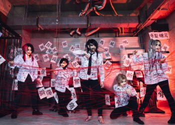 The photo shows the visual kei band GERTENA in a space with an industrial feel, decorated with a multitude of red strings and small pieces of white papers and kanji on them. All band members are dressed in black and white clothing decorated with ink splats.