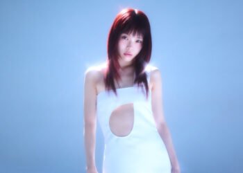 Photo shows AiNA THE END in a white dress with cutouts, posing in front of a blue background and standing in a spotlight. © Avex