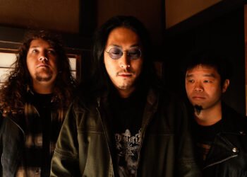 The photo features the three men of the band Hebi Katana standing in a Japanese traditional room in natural lighting. They are standing close together and are all wearing dark-coloured clothing. Photo by Hiromi Furukawa