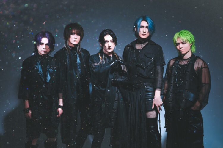 The photo shows a five members of the visual kei band Matenrou Opera. They are standing together closely, all dressed in black outfits. The background is also dark and it appears that there is a presence of bokeh.