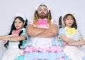 The three members of BABYBEARD, dressed in colourful dresses, in light/pastel pink, blue and green, with puffy short sleeves and bows, are standing next to each other while having their arms crossed. LADYBEARD (in pink) stands in the centre of the photo, Suzu (green) on the left and Mizuki (blue) on the right.