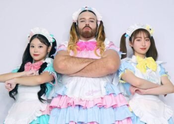 The three members of BABYBEARD, dressed in colourful dresses, in light/pastel pink, blue and green, with puffy short sleeves and bows, are standing next to each other while having their arms crossed. LADYBEARD (in pink) stands in the centre of the photo, Suzu (green) on the left and Mizuki (blue) on the right.